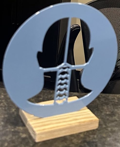 Powder-coated light blue steel logo piece standing on a wooden base
